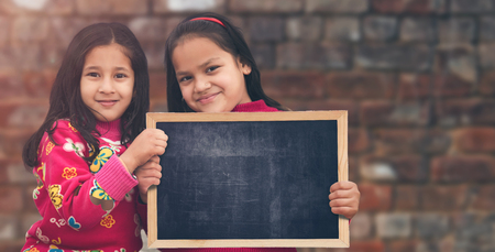 Two Happy Indian Little girl standing holding chalkboard slate, looking directly at camera. selective focus.の写真素材