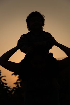 A silhouette of a happy young girl child the arms of his loving mother for a hug, in front of the sunset in the sky on a summer day.の写真素材