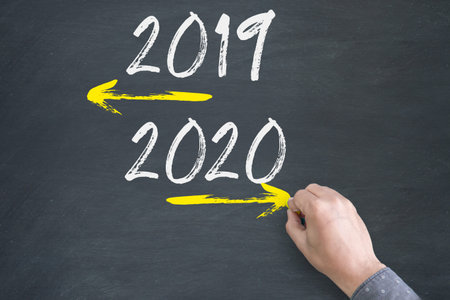 Close-up of human hand drawing old Year 2019 and New Year 2020 with arrow on Blackboard Background