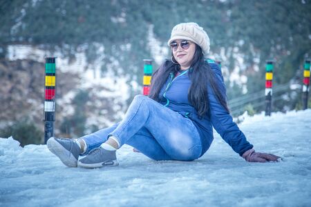 Portrait of an Indian woman wearing woolen cap and jacket enjoying snowfall and feeling amazed in a snowy eveningの写真素材