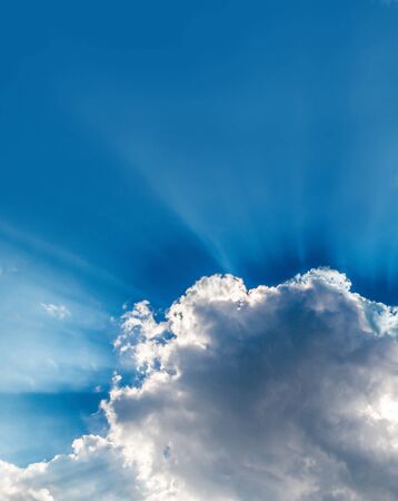 Sun rays bursting through clouds in a blue sky.の写真素材