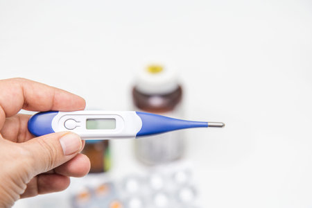 Electronic thermometer with tablets and capsules on a white background - protection against...