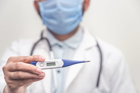 Doctor wearing stethoscope holds digital medical thermometer to measure the body temperature,...
