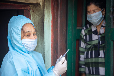 Young woman doctor in PPE protective mask and gloves holding a syringe and  vaccine, standing with village women explaining importance of  virus vaccine. The concept of a new vaccine against the disease, flu vaccine vaccinationの写真素材