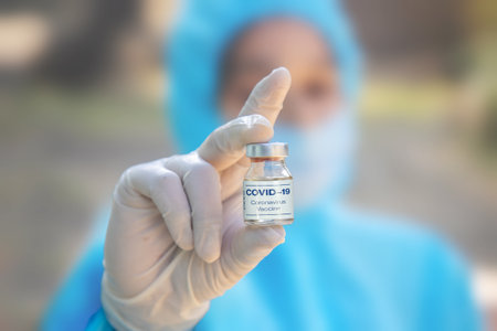 Young woman doctor in PPE protective mask and gloves holding a syringe and  vaccine. The concept of a new vaccine against the disease, flu vaccine vaccinationの写真素材