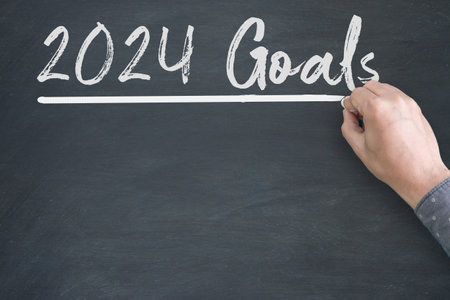 2024 Goals new year. A male hand writing new year goals on chalkboard.の写真素材