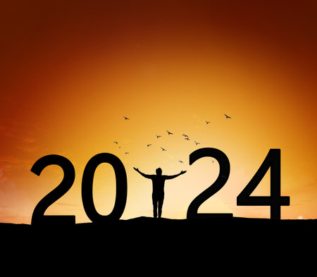 Young man standing Silhouette over mountain against orange sky to 2024 new year, New year conceptの写真素材