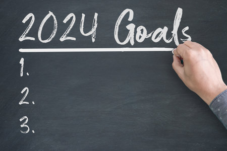 2024 Goals new year. A male hand writing new year goals on chalkboard.の写真素材