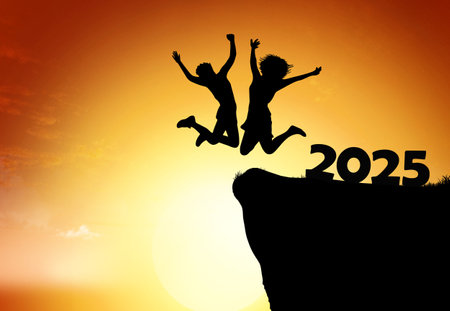 A person leaps into the air with raised arms at the edge of a cliff against a vibrant sunset, symbolizing excitement and new beginnings for the year 2025.の写真素材