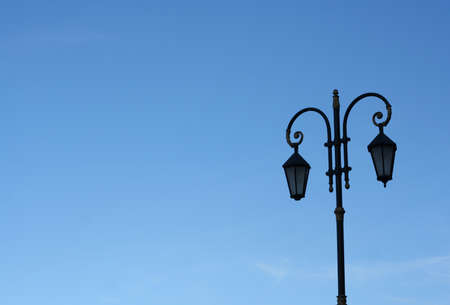 Old doubled street lamppost  against the blue skyの写真素材