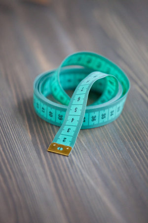 Sewing accessories â€“ the green centimetric measuring tape, tailor measure tape on a wooden...