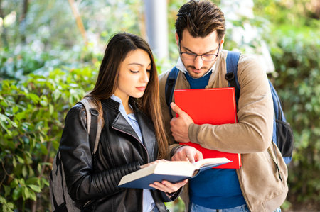 Two students, male and female, talking outdoors holding booksの写真素材