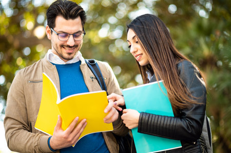 Two students, male and female, talking outdoors holding booksの写真素材