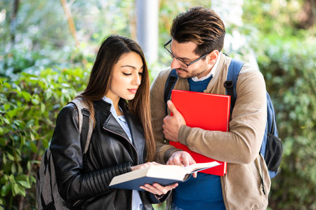 Two students, male and female, talking outdoors holding booksの写真素材