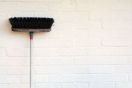 A old broom leaning against a painted brick wall.の写真素材