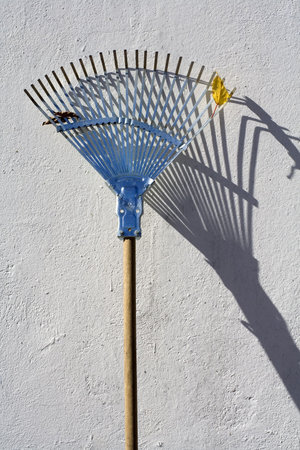 A rake standing against a white wall in the sun.
