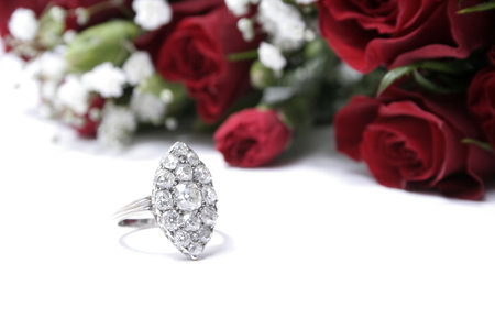 A single diamond and white gold ring on a white background with roses. 