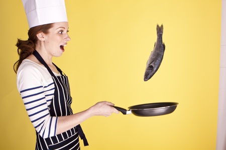 A young attractive female chef flipping a fish in a pan. の写真素材