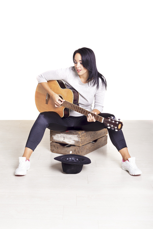 Young female busker sitting on a wooden box playing her guitar for money.の写真素材