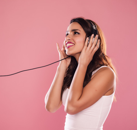 Young woman listening to music over a pink background.の写真素材