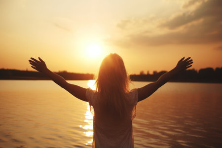 Young woman with arms outstretched against sunset on the river bank.の素材