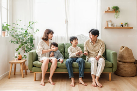 Family of four sitting on a green couch in a bright living roomの素材