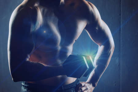 Man holding a dumbbell doing a fitness workout backlitの写真素材