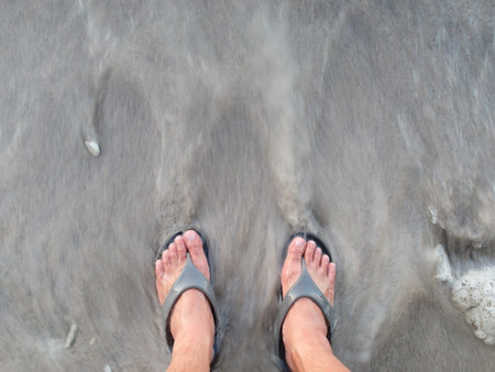 Man with flipflop on the beach with wave rushing back to the seaの写真素材