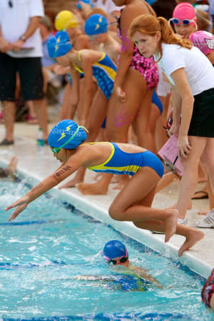 Lawrenceville, GA, USA - June 14:  A female youth swimmer dives into pool to swim her leg of a relay race during a neighborhood swim meet between three swim teams.のeditorial素材