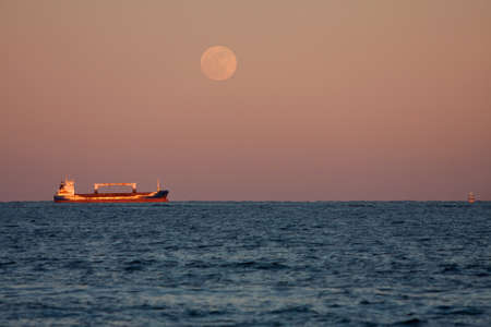 A Cargo Ship Sits Anchored Off Florida Coast Under Full Moonの写真素材