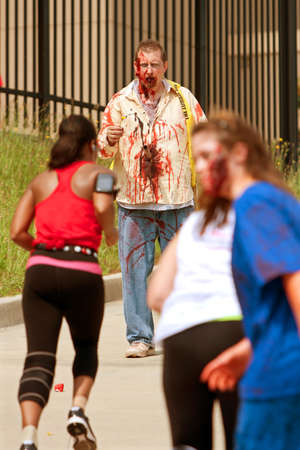 Atlanta, GA, USA - June 8, 2013:  A blood soaked zombie waits for runners to get closer, as they move through the course at the Atlanta Zombie Run. Hundreds of runners dodged zombies in the 5K race.のeditorial素材