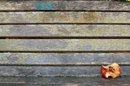 Eaten apple core sits on empty park benchの写真素材