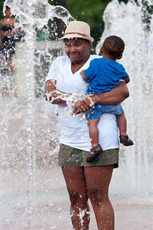Atlanta, GA, USA - September 6, 2014:  A woman stands holding a toddler while water squirts all around her in the fountain at Centennial Park in Atlanta.のeditorial素材