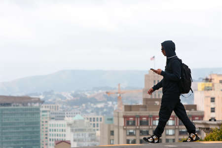 San Francisco, CA, USA - May 18, 2015:  A young adult male listens to his smart phone as he crosses a street overlooking a steep dropoff in the Knob Hill area of San Francisco.のeditorial素材