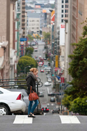 San Francisco, CA, USA - May 18, 2015:  The steep hills of San Francisco are evident as a young woman crosses a street overlooking a severe dropoff, in the Nob Hill area of the city.のeditorial素材