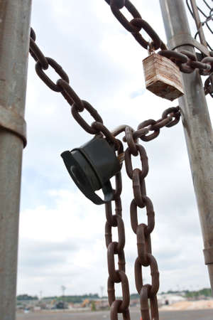 Padlocks and chains secure gate to industria work areaの写真素材