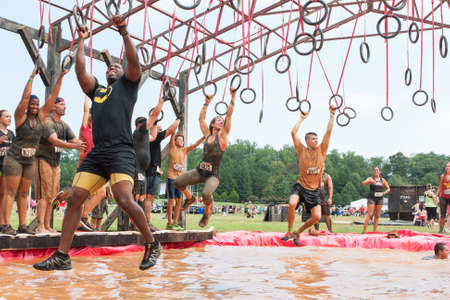 Conyers, GA, USA - August 22, 2015:  Competitors try to cross a muddy pool of water by swinging from rings at the Rugged Maniac Obstacle Course race in Conyers, GA.のeditorial素材