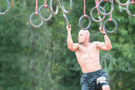 Conyers, GA, USA - August 22, 2015:  A young fit male swings from rings suspended from wood beams to...