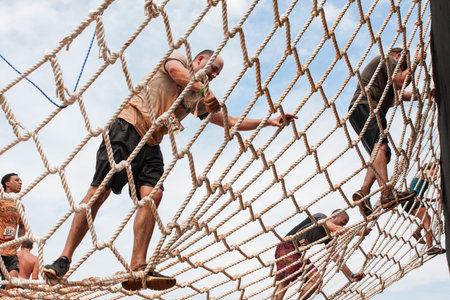 Conyers, GA, USA - August 22, 2015:  Competitors climb a cargo net on their way to the next obstacle...