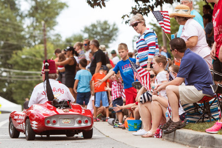 Alpharetta, GA, USA - August 1, 2015:  Families sit on curb with American flags and interact with participants along the parade route of the Old Soldiers Day Parade in Alpharetta, GA on August 1, 2015.のeditorial素材