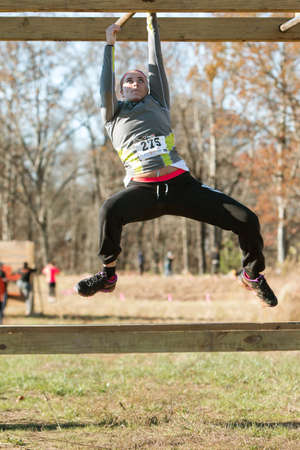 Buford, GA, USA - November 21, 2015:  A young woman grips a metal bar as she tries to pull herself across an obstacle while suspended over the ground, at the Muddy Brute Challenge in Buford, GA on November 21, 2015.のeditorial素材