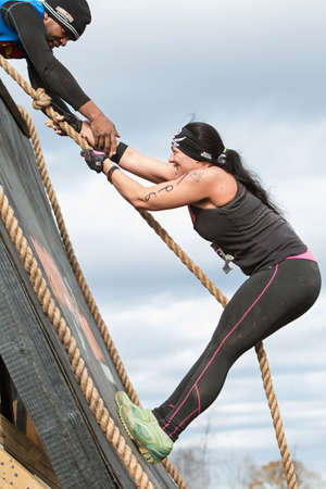 Buford, GA, USA - November 21, 2015:  A woman struggles to climb up a wall obstacle using a rope at the Muddy Brute Challenge in Buford, GA on November 21, 2015.のeditorial素材