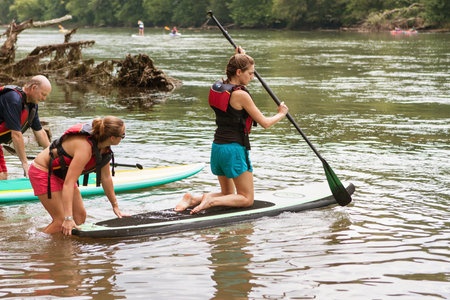 Atlanta, GA, USA - July 25, 2015:  A young woman kneels on a paddleboard as she gets a push into the Chattahoochee River on a hot summer day on July 25, 2015 in Atlanta, GA.のeditorial素材