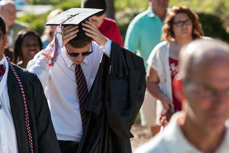 Athens, GA, USA - May 13, 2016:  A male graduate adjusts his mortar board and tassle as he walks toward the graduation ceremony at the University of Georgia on May 13, 2016 in Athens, GA.のeditorial素材