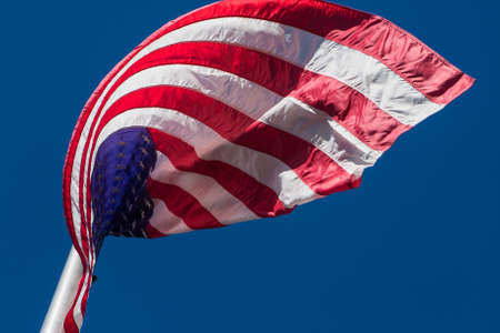 An American flag curls in interesting pattern as wind blows it on flag pole.の写真素材