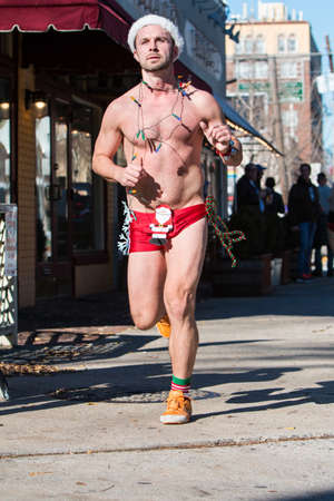 Atlanta, GA, USA - December 10, 2016:  A male runner wearing Christmas lights, a Santa hat and a skimpy swimsuit jogs down a city street at the Santa Speedo Run, an annual charity fundraiser, on December 10, 2016 in Atlanta, GA.のeditorial素材