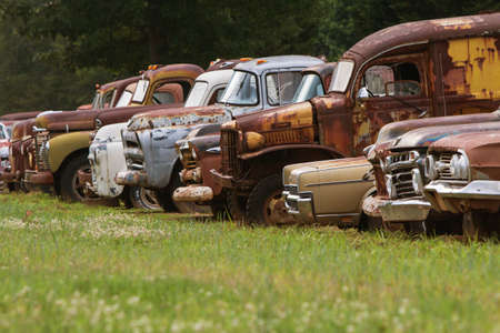 Gainesville, GA, USA - June 1, 2017:  A row of old, discarded cars and trucks sit lined up all in a row in a grassy junkyard field on June 1, 2017 in Gainesville, GA.のeditorial素材