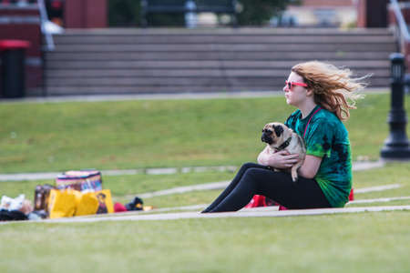 Suwanee, GA, USA - May 6, 2017:  A young woman lovingly holds her pug dog while sitting on the grass at Woofstock, a dog festival at Suwanee Town Center on May 6, 2017 in Suwanee, GA.のeditorial素材