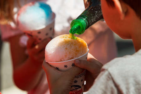 Suwanee, GA, USA - May 6, 2017:  A bottle pours green syrup onto a snow cone that a child is holding at Woofstock, a dog festival at Suwanee Town Center on May 6, 2017 in Suwanee, GA.のeditorial素材
