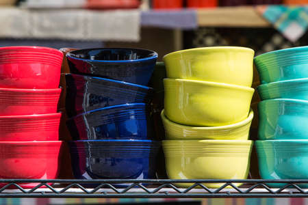 Brightly colored ceramic bowls are stacked on a shelf for sale at an antique festival.の写真素材